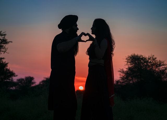 Muž a žena sa držia za ruky, stoja oproti sebe na skale pri západe slnka.jpg