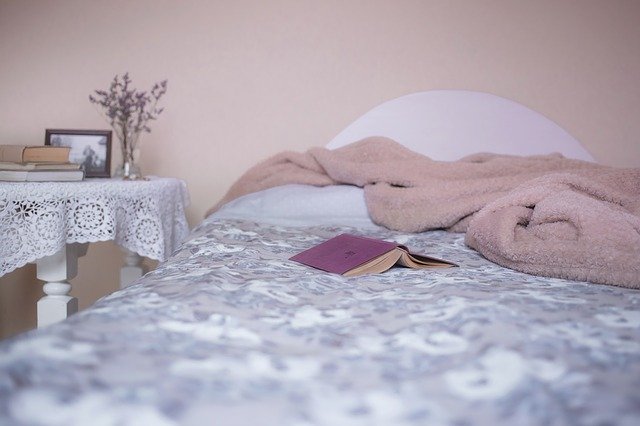 Posteľ zakrytá dekou, na ktorej je položená ružová kniha.jpg