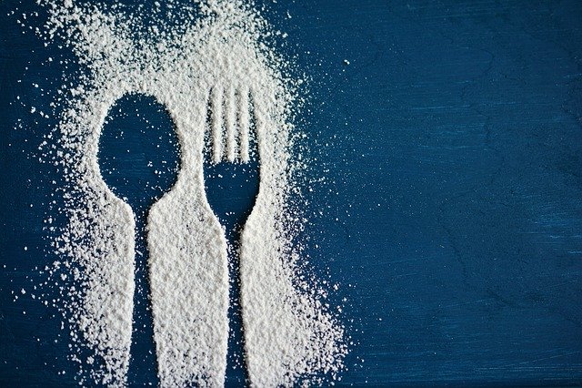 Obrys vidličky a lyžičky obsypané cukrom na modrom stole.jpg